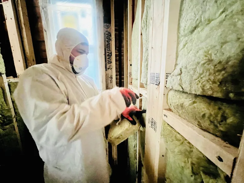 Installer fitting ROCKWOOL stone wool batts into a wood-framed wall