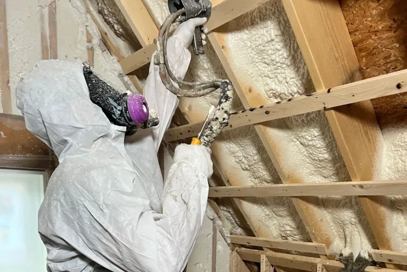 Installer in a protective suit spraying foam insulation onto attic rafters